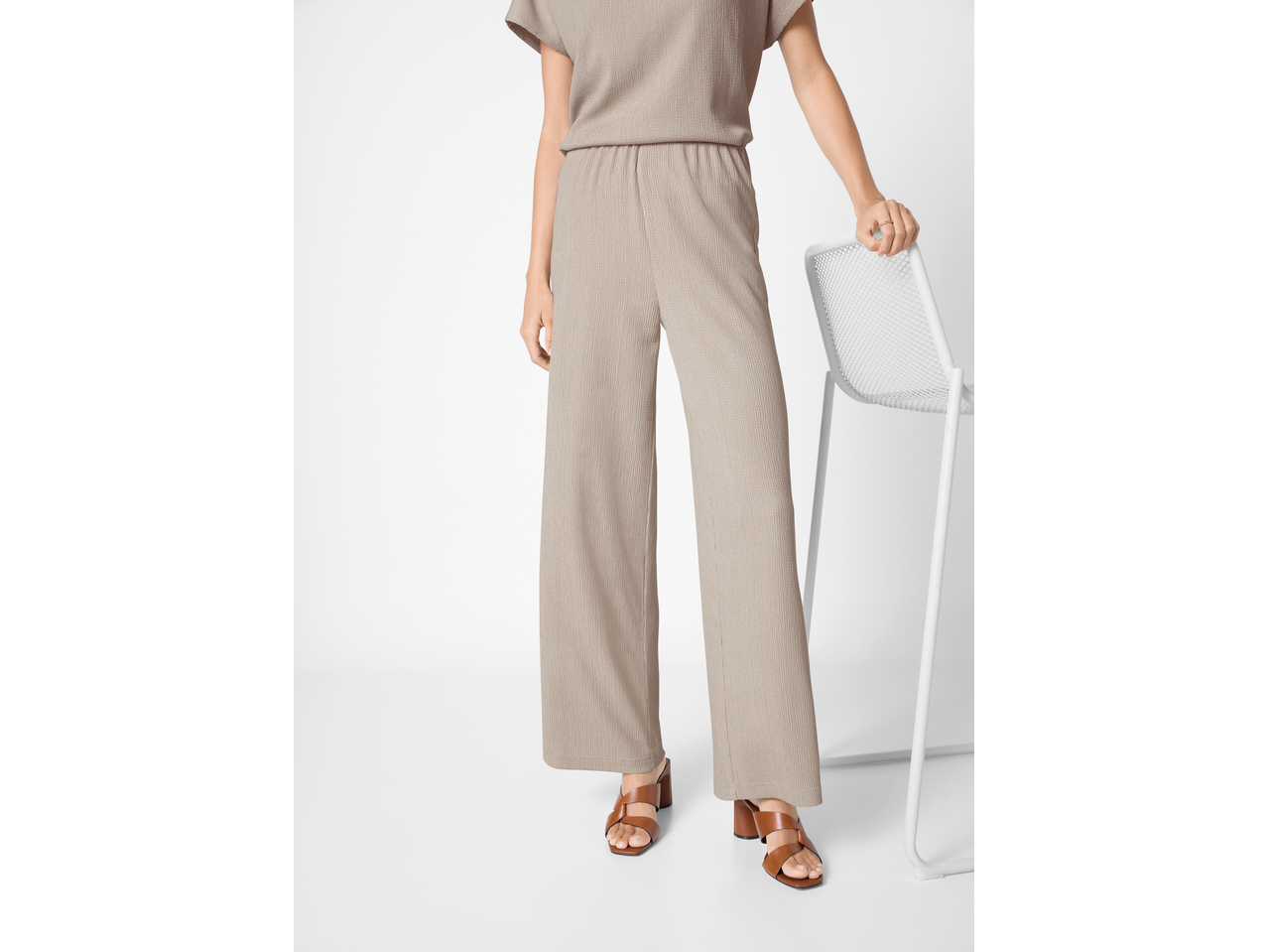 Žena u bež širokim hlačama i finom pletenom topu ESMARA, sa smeđim sandalama.