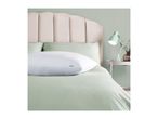 White pillow on a bed with light green duvet and pillows, with a pink headboard.