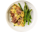Two Irish beef medallion steaks, sliced and drizzled with sauce, served with mashed potatoes and asparagus.