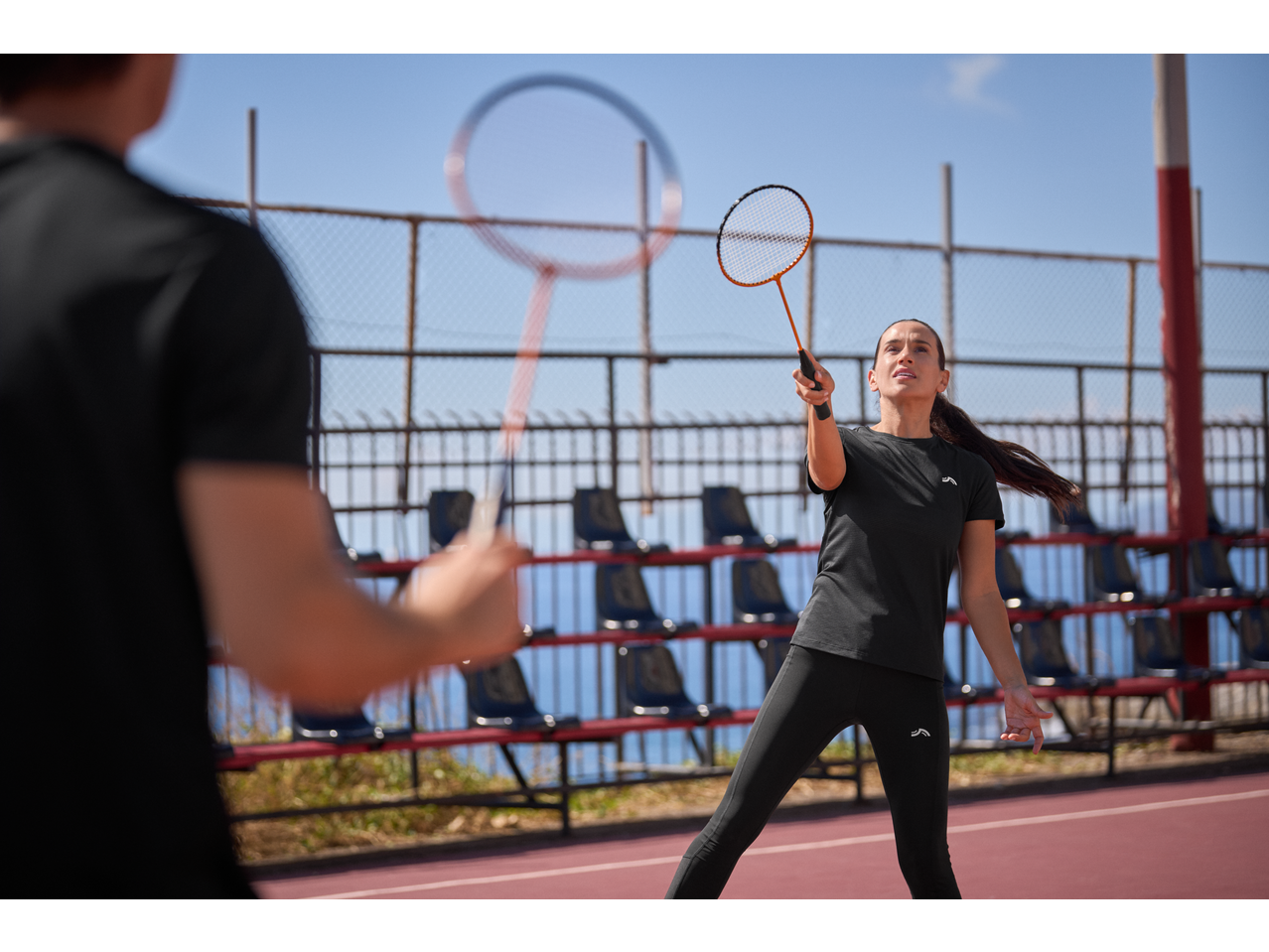 Two people playing badminton with CRIVIT badminton rackets on an outdoor court.