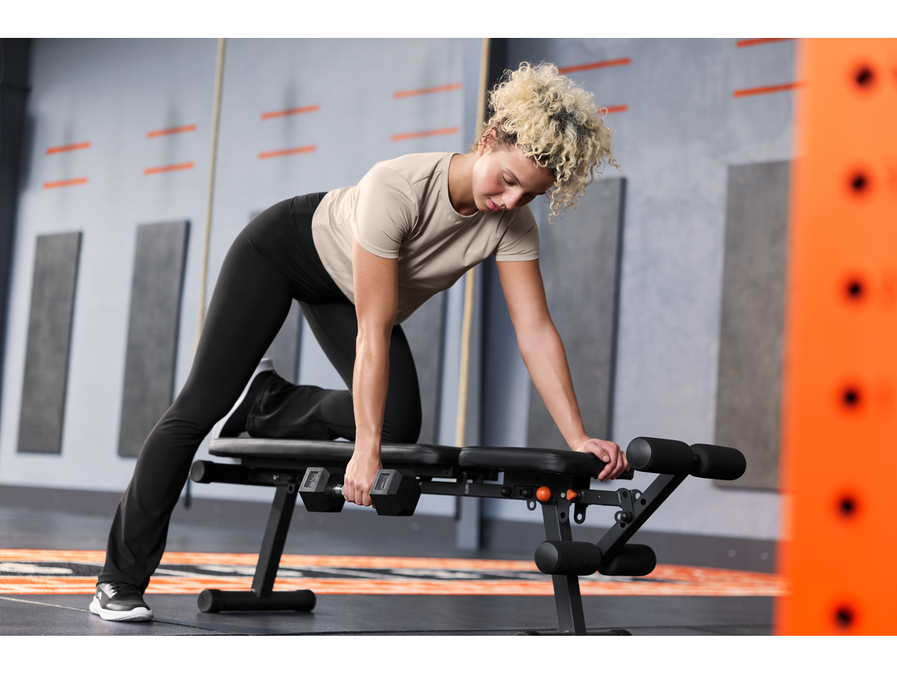 Woman in CRIVIT short sleeve sports top and leggings doing dumbbell rows on a bench.