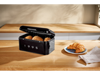 Black bread box with bread rolls and a croissant on a wooden counter.