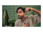 Man in a bathrobe trimming his hair with a hair clipper in a bathroom.