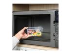 A hand placing a plastic food container with noodles and vegetables into a microwave