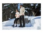 A man and a woman in warm winter clothing standing in a snowy forest.