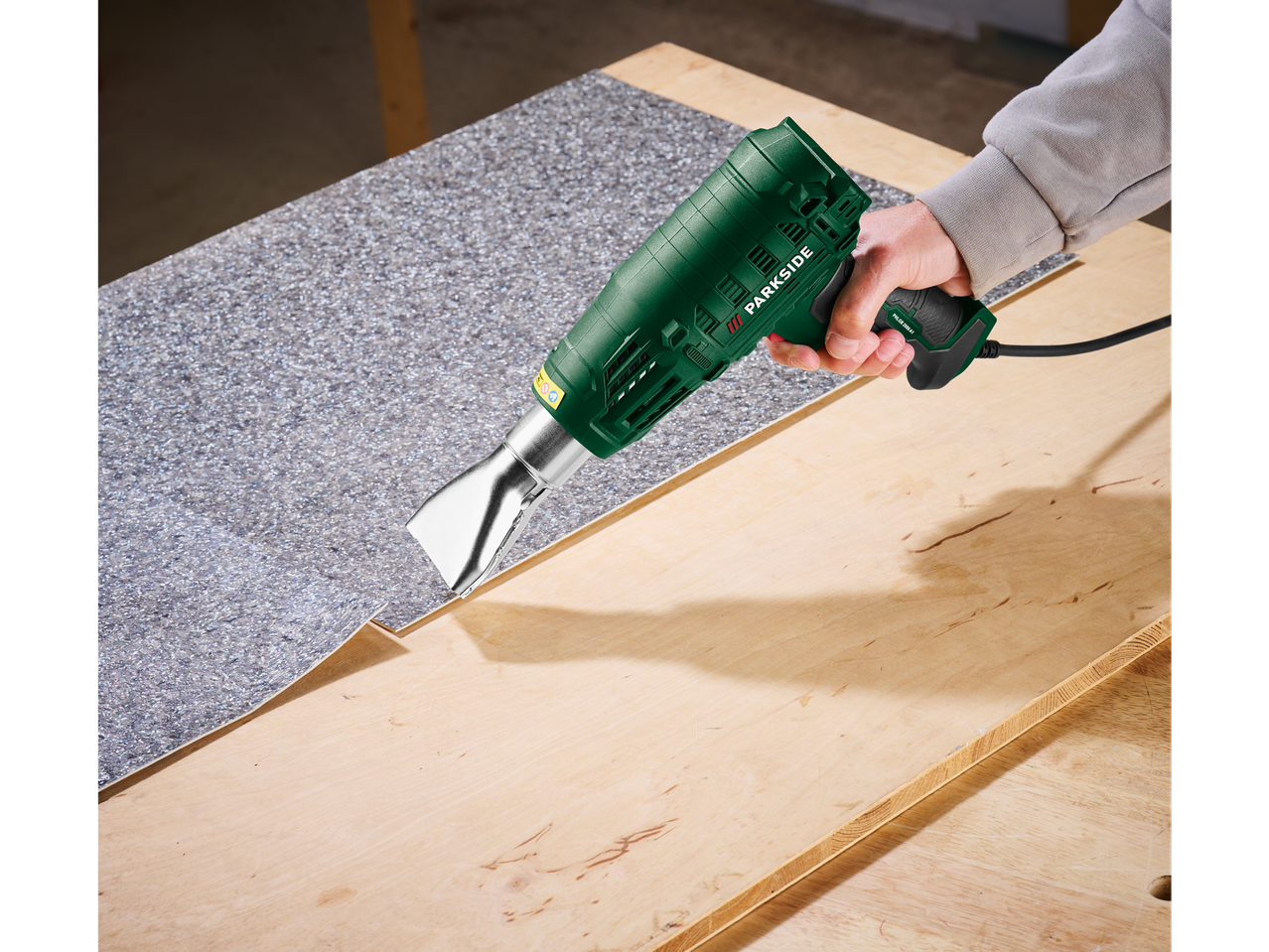 Мъж използва пистолет за горещ въздух Parkside за премахване на подова настилка.