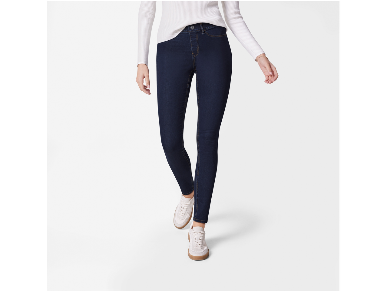Woman wearing dark wash skinny jeans, a white ribbed sweater, and white sneakers.