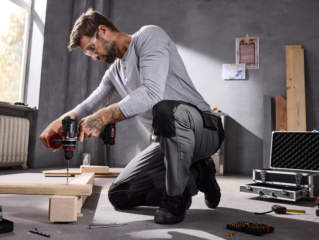Мъж в работно облекло пробива дървена дъска с акумулаторна бормашина.