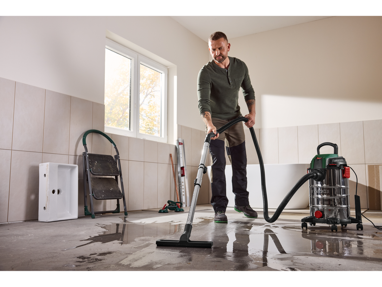 Bărbat curățând apă cu un aspirator într-o baie în construcție.
