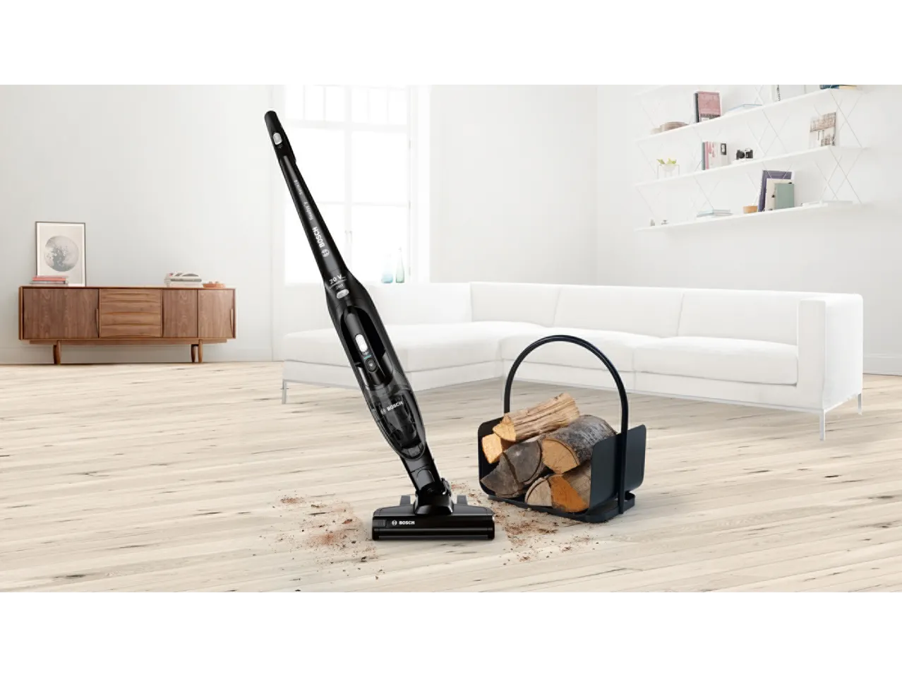Bosch 2-in-1 stick vacuum cleaner cleaning a wooden floor with scattered dirt next to a log basket.