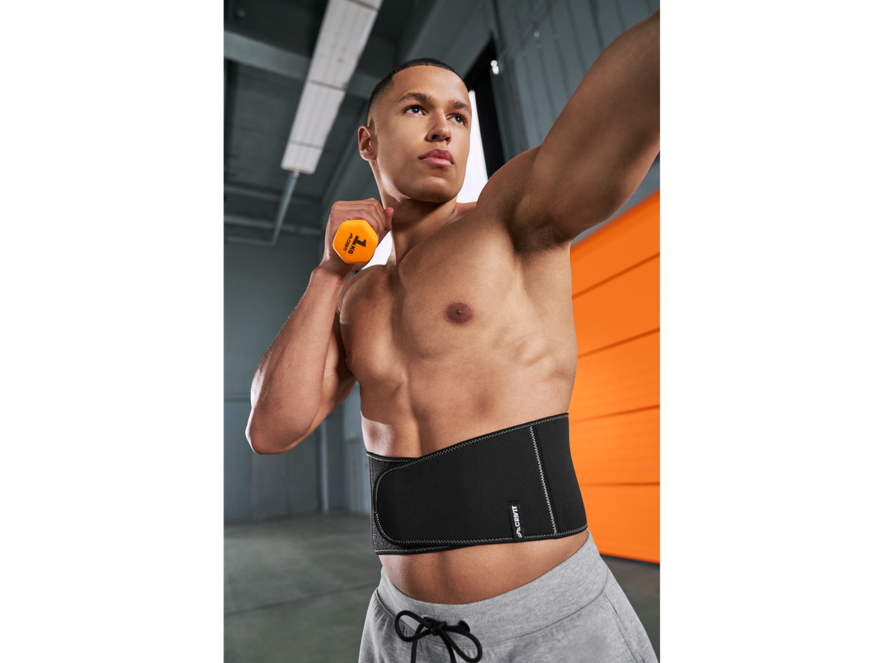 Άνδρας γυμνάζεται με πορτοκαλί βαράκι και μαύρη αθλητική ζώνη μέσης.