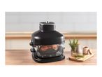 Black air fryer with a transparent basket containing food, on a wooden table with herbs and spices.