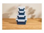 Stack of four collapsible blue food storage containers with white lids on a wooden surface.