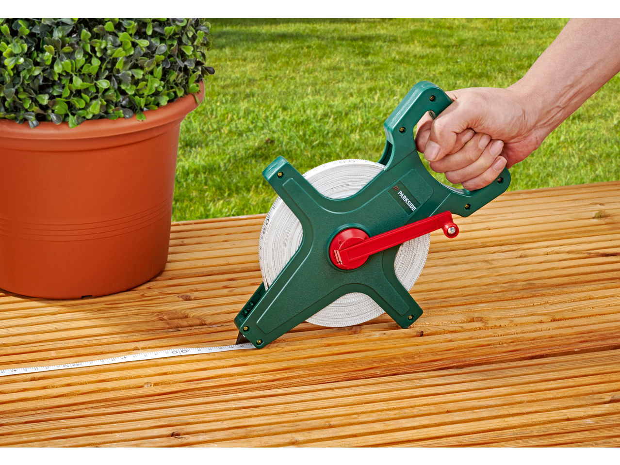 Bandă de măsurat PARKSIDE pe o terasă din lemn, lângă un ghiveci cu plante.