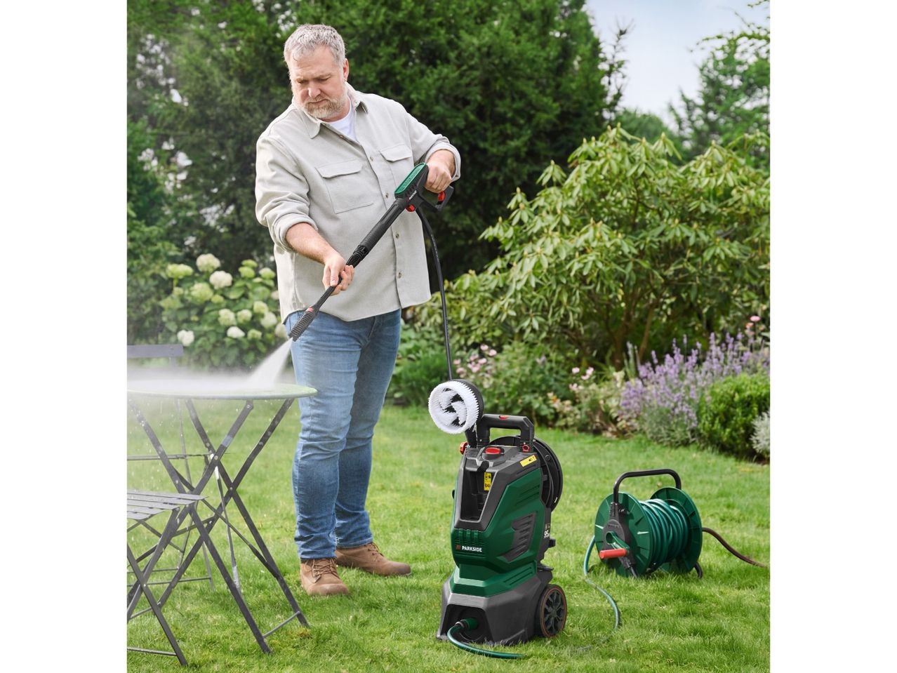 Man pressure washing a garden table with a pressure washer and hose reel in a garden.