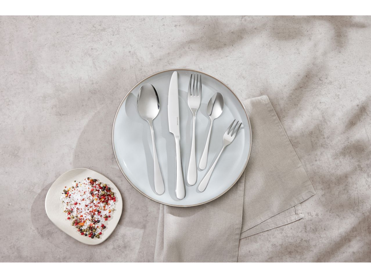 Silver Cutlery Set on a plate, with a small dish nearby.