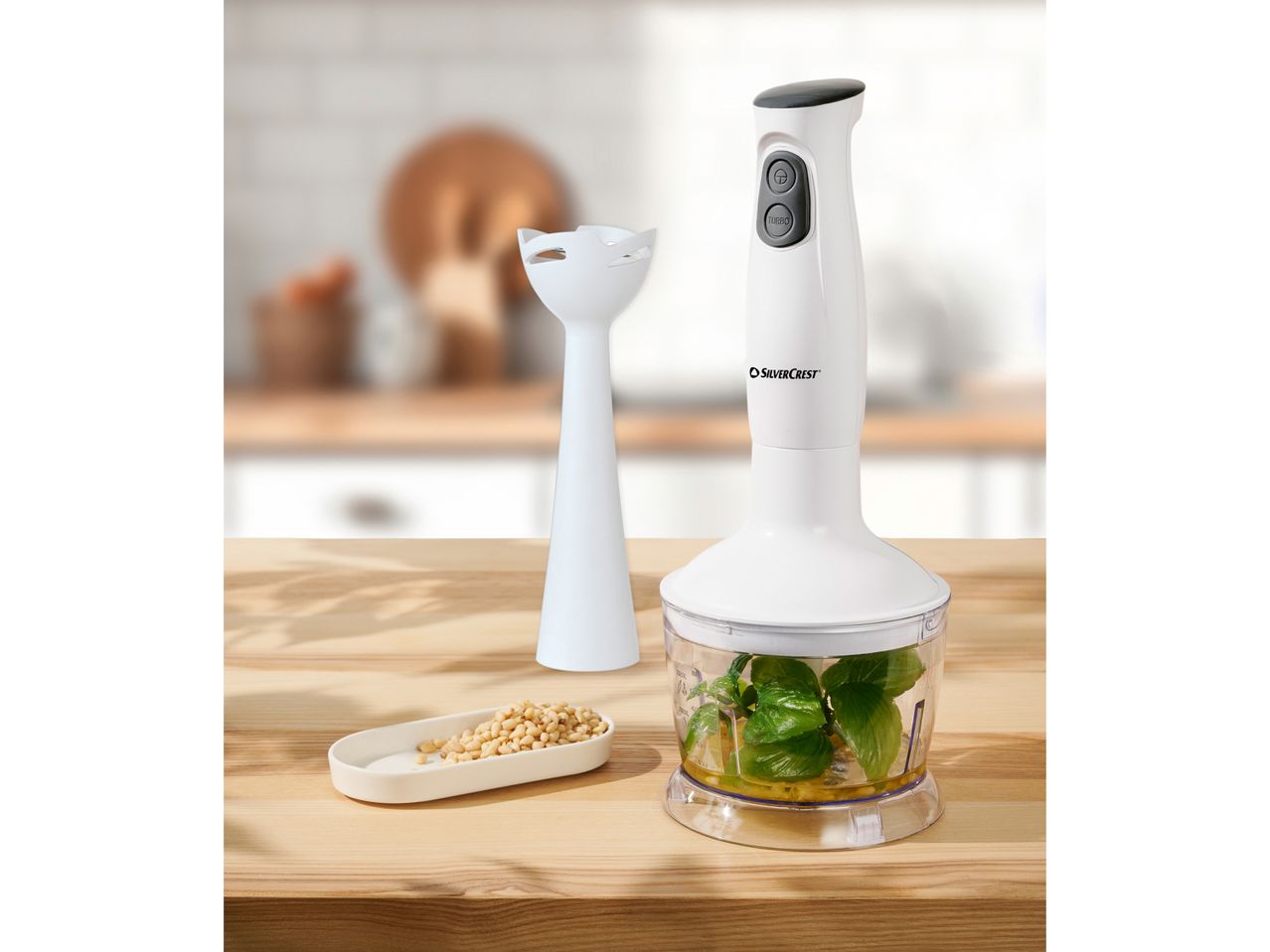 SilverCrest hand blender with a chopper attachment containing basil and oil, next to pine nuts.