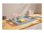 A breakfast tray with a coffee mug, pastry, and flower on a wooden counter.