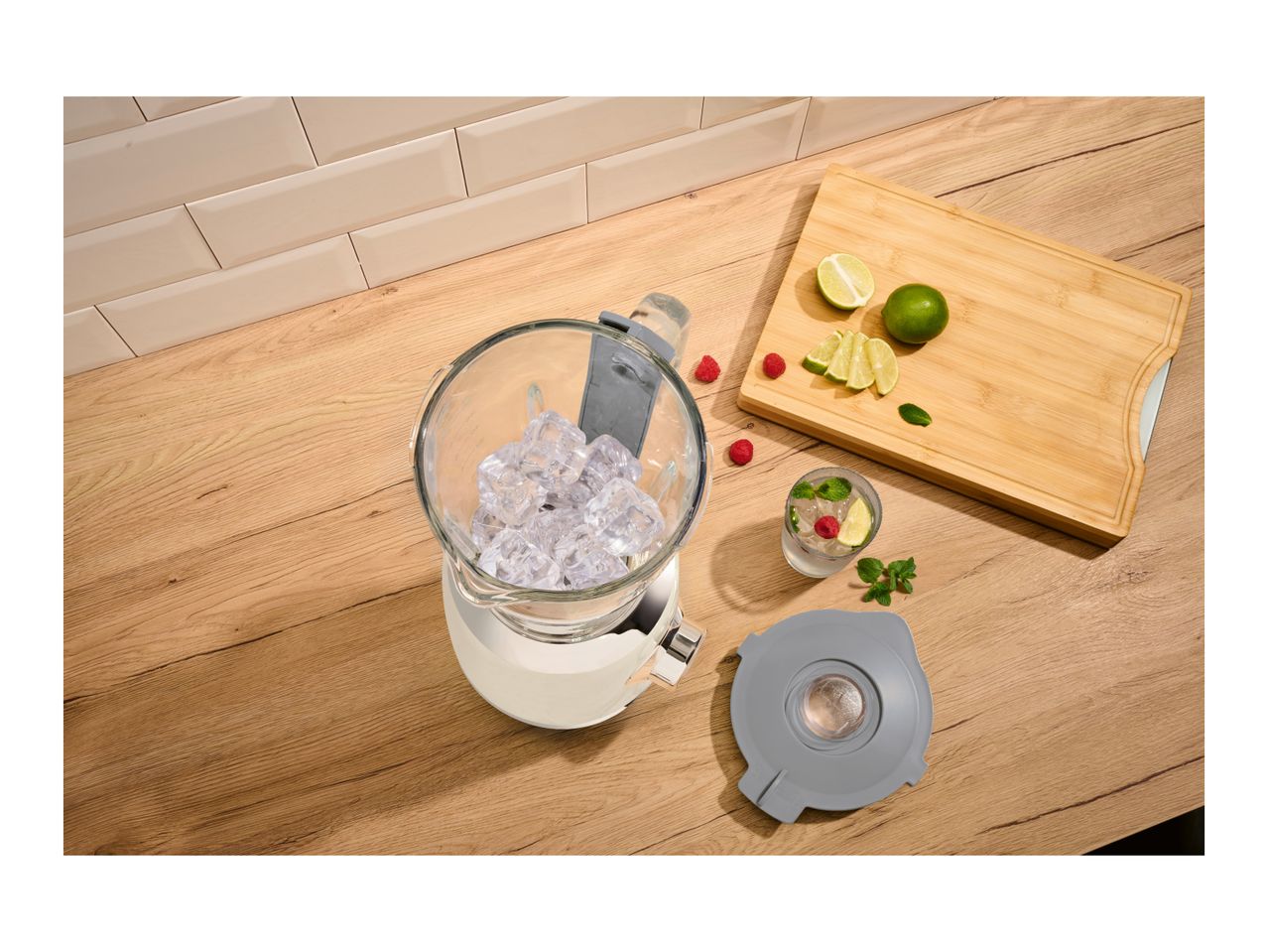 A white blender filled with ice cubes on a wooden countertop next to fresh ingredients.