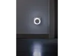 A white circular night light plugged into a wall socket, illuminating a dark room.