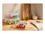 Glass food storage containers with fresh vegetables and pasta salad on a wooden kitchen counter.