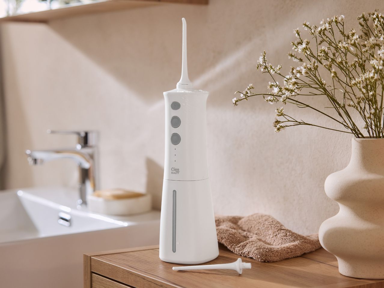 White cordless water flosser with a vase of flowers and a sink in a bathroom setting.