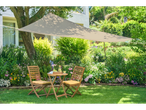 Beige garden shade sail, outdoor wooden table and chairs.