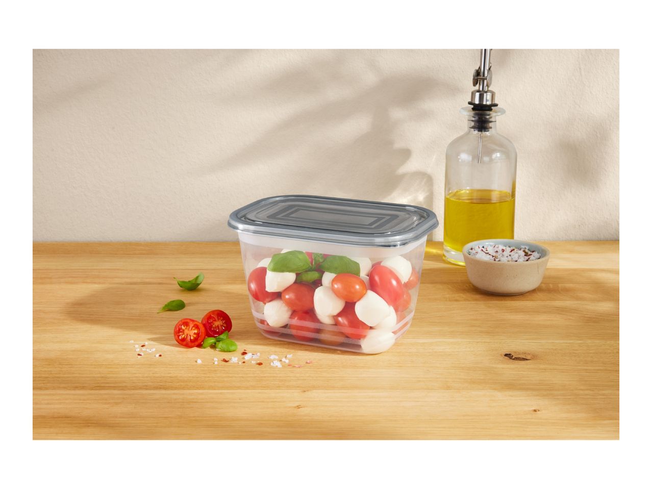 A clear food storage container filled with cherry tomatoes, mozzarella balls, and basil.