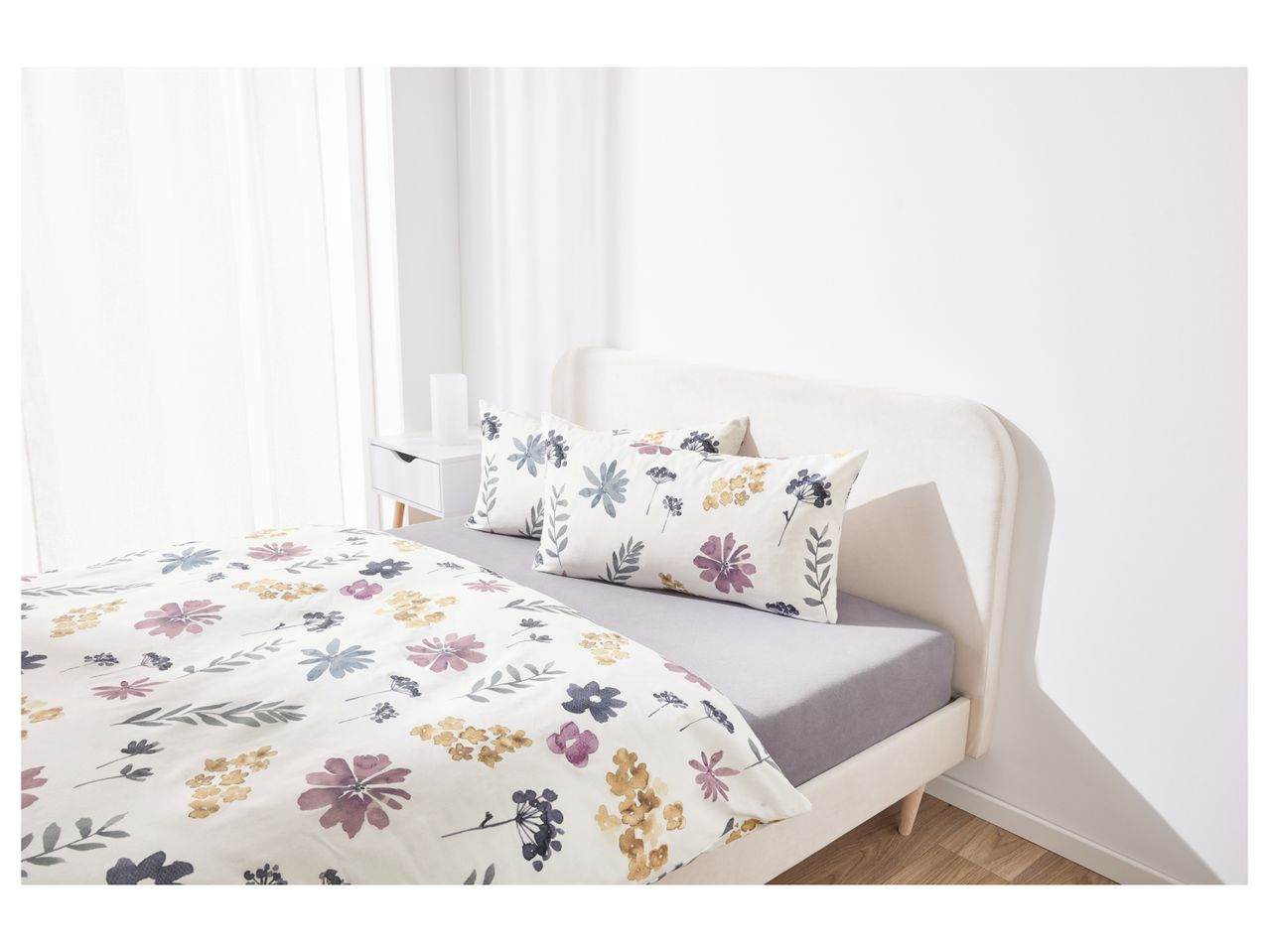 A bed with floral duvet cover and pillows, and a white nightstand.