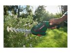 Hand holding a green and black cordless hedge trimmer, pruning a rosemary bush with purple flowers.