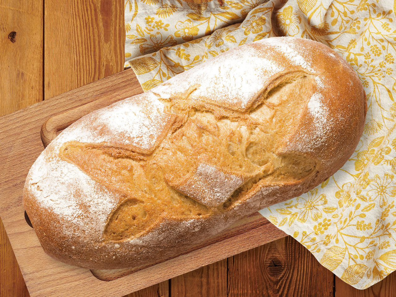 Прясно изпечен хляб, поръсен с брашно, върху дървена дъска и жълта кърпа.