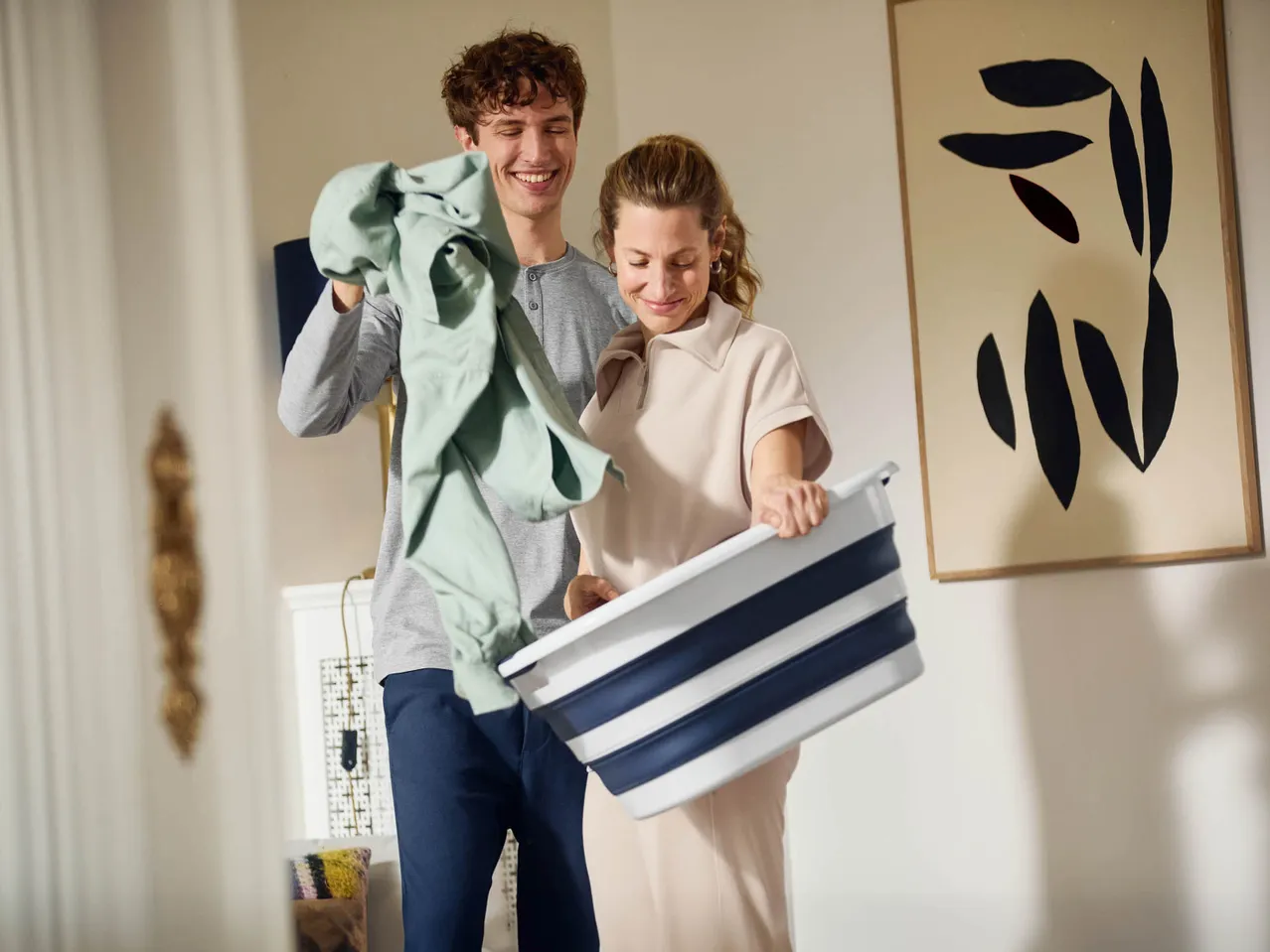 Un uomo e una donna sorridono mentre mettono i vestiti in una cesta per il bucato pieghevole.