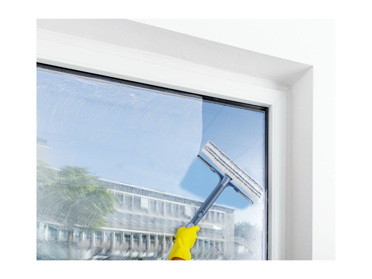A person in yellow gloves cleaning a window with a window squeegee, leaving streaks of soap.