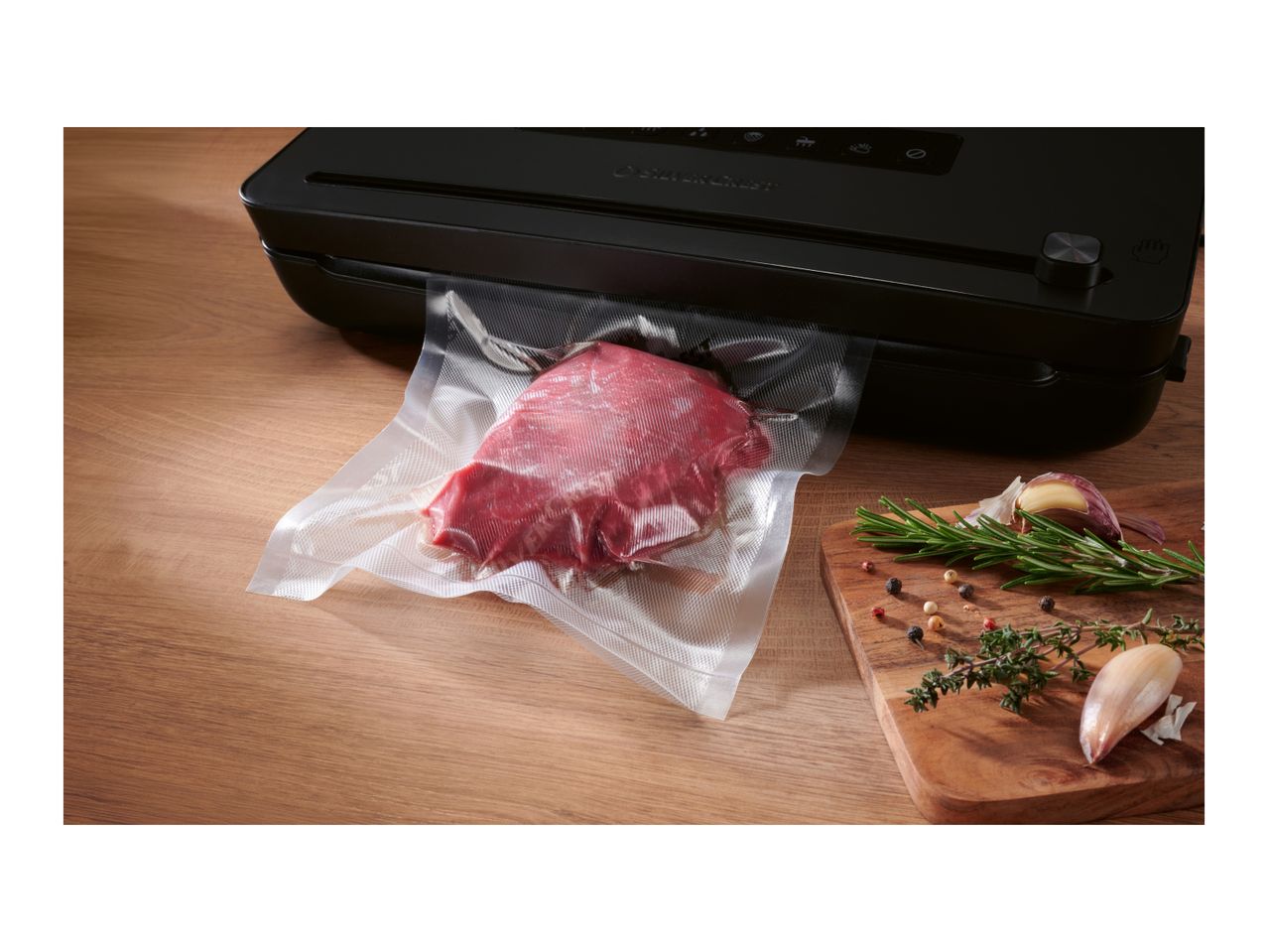 A vacuum sealer packaging a piece of raw meat on a wooden table next to fresh herbs.