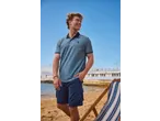 Man in blue polo shirt and navy shorts on a beach with a deckchair