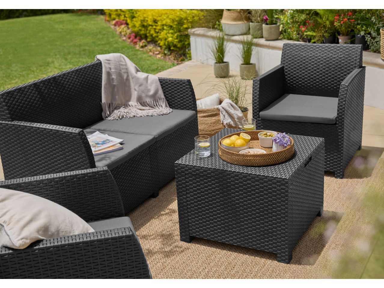 Outdoor patio furniture set with black wicker sofa, armchair, and coffee table on a rug.