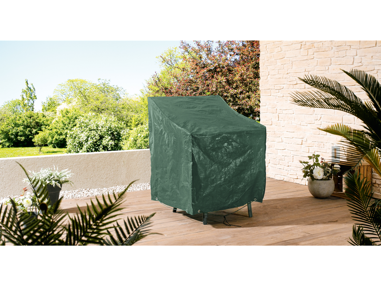 A green protective cover on a patio chair on a wooden deck with plants and a stone wall.
