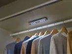 LED closet light illuminates sweaters hanging on wooden hangers.