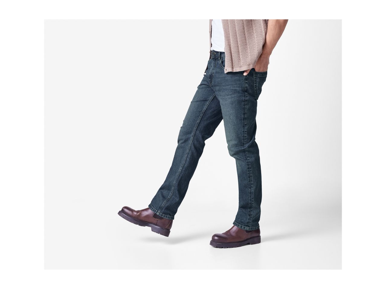 Man wearing blue jeans, a white t-shirt, a beige cardigan, and brown boots.