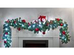 Christmas garland with red baubles and white lights draped over a white fireplace, with gifts.