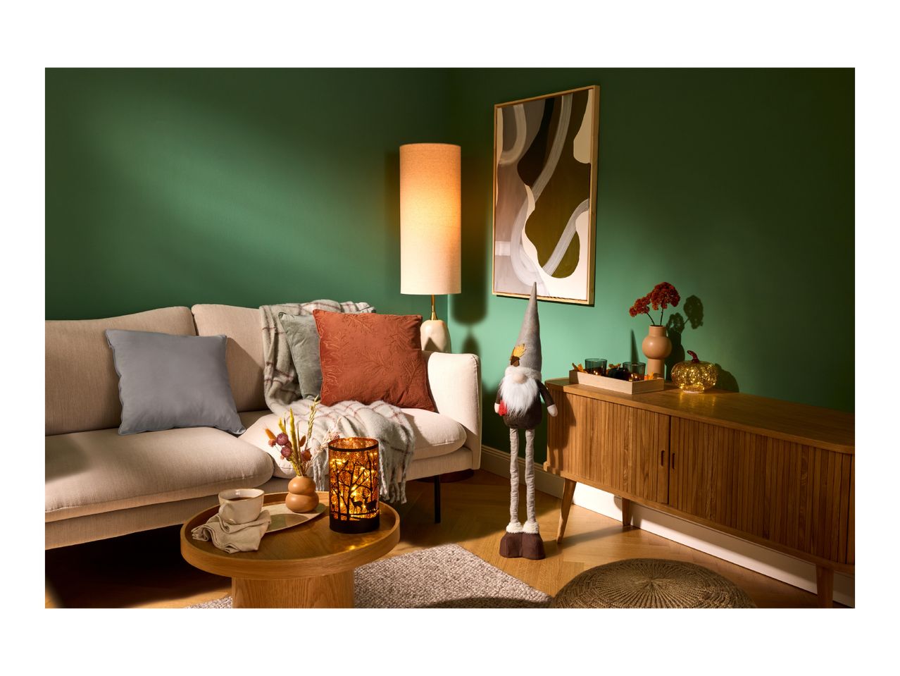 Living room with a beige sofa, floor lamp, wooden cabinet, and autumn decorations.