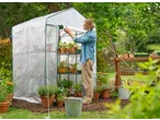 Woman opening a Parkside® Greenhouse filled with potted plants in a garden.