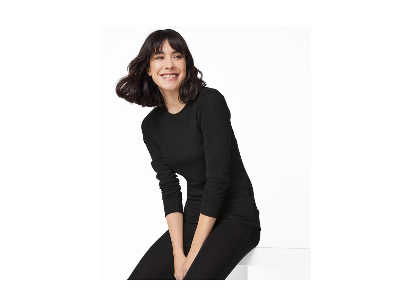 A woman in a black long-sleeved top and black leggings smiles while sitting.