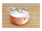 Copper-colored cooking pot with a stainless steel lid and handles on a wooden surface.