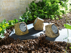 Three solar-powered rock lights illuminate a garden path.