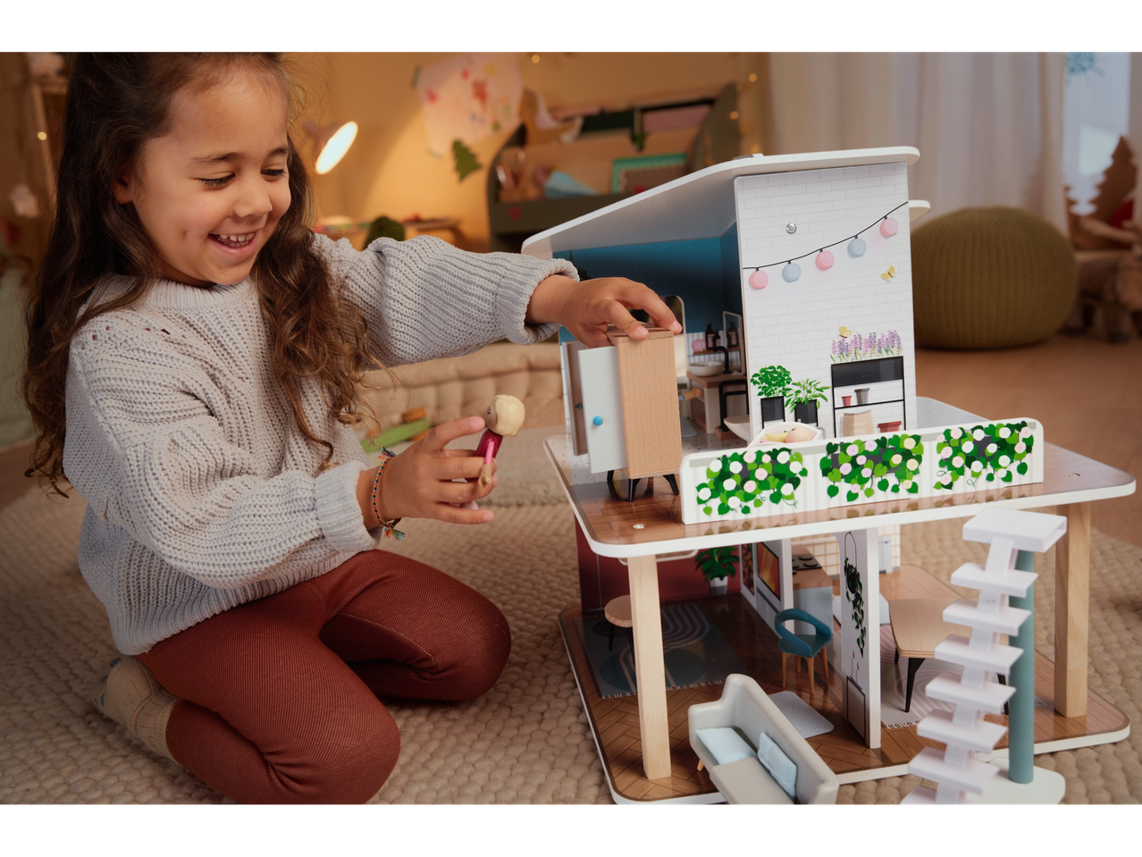 A smiling child plays with a Playtive Doll House, moving a doll inside.