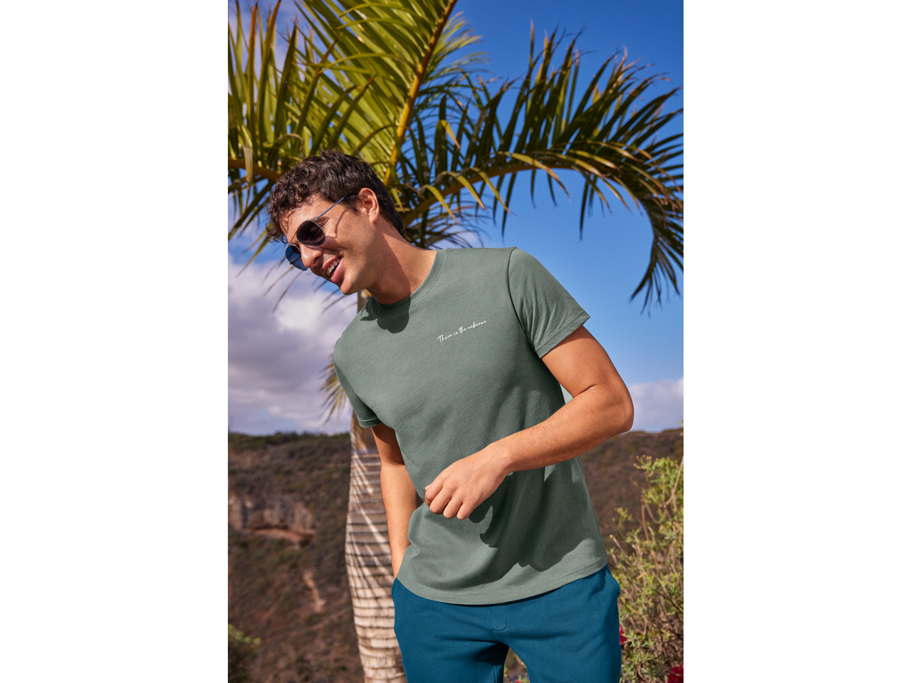 Man in a green t-shirt with 'Thrive in the unknown' text and blue shorts outdoors.