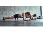Two people in athletic wear doing planks on a gym floor.