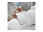 Hands placing a white pillow protector with a grey trim onto a bed.