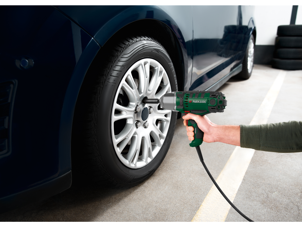 Inimene kasutab Parkside® elektrilist löökmutrivõtit auto rehvi vahetamiseks.